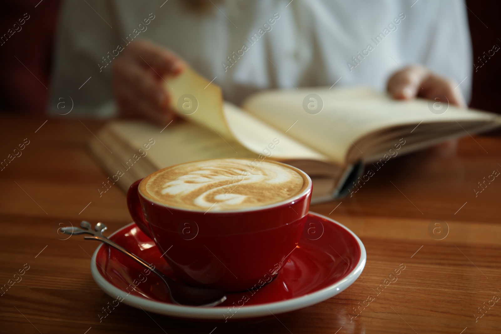 Photo of Woman with coffee reading book indoors, focus on cup