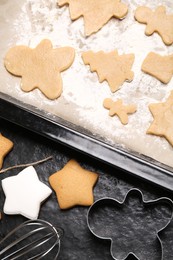 Raw and cooked Christmas cookies with cutters on dark table, flat lay