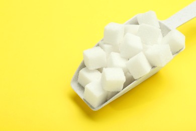 Photo of White sugar cubes and scoop on yellow background