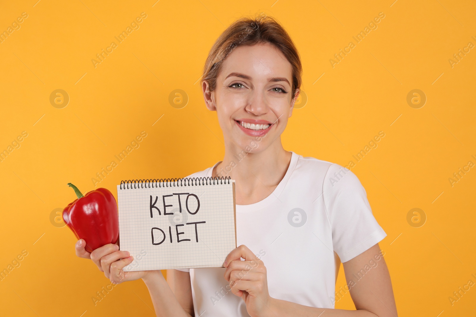 Photo of Woman holding notebook with phrase Keto Diet and bell pepper on yellow background