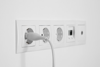 Photo of Many power sockets with plug, ethernet and TV coax plates on white wall indoors