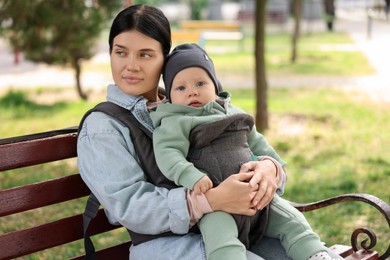 Photo of Mother holding her child in sling (baby carrier) on bench in park