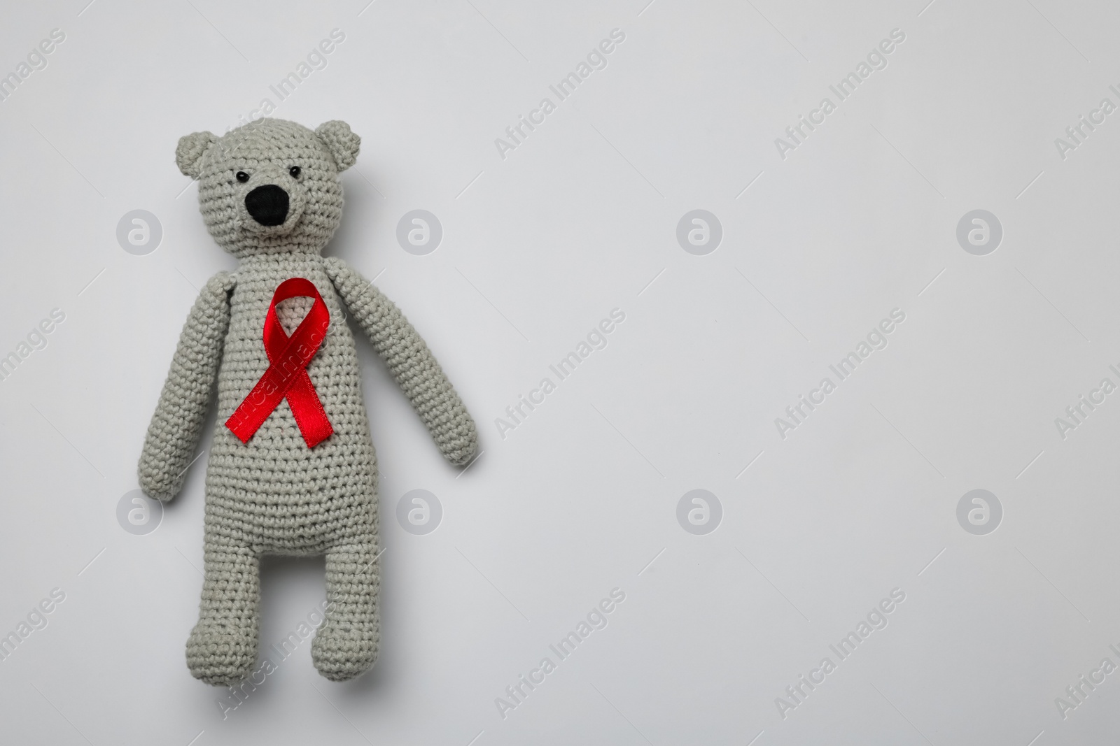 Photo of Cute knitted toy bear with red ribbon on light grey background, top view and space for text. AIDS disease awareness