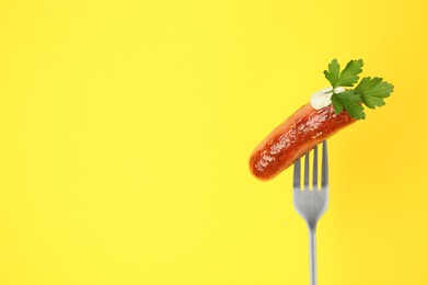Photo of Fork with tasty fried sausage, mayonnaise and parsley on yellow background. Space for text