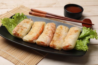 Photo of Delicious fried spring rolls, sauce and chopsticks on light wooden table, closeup