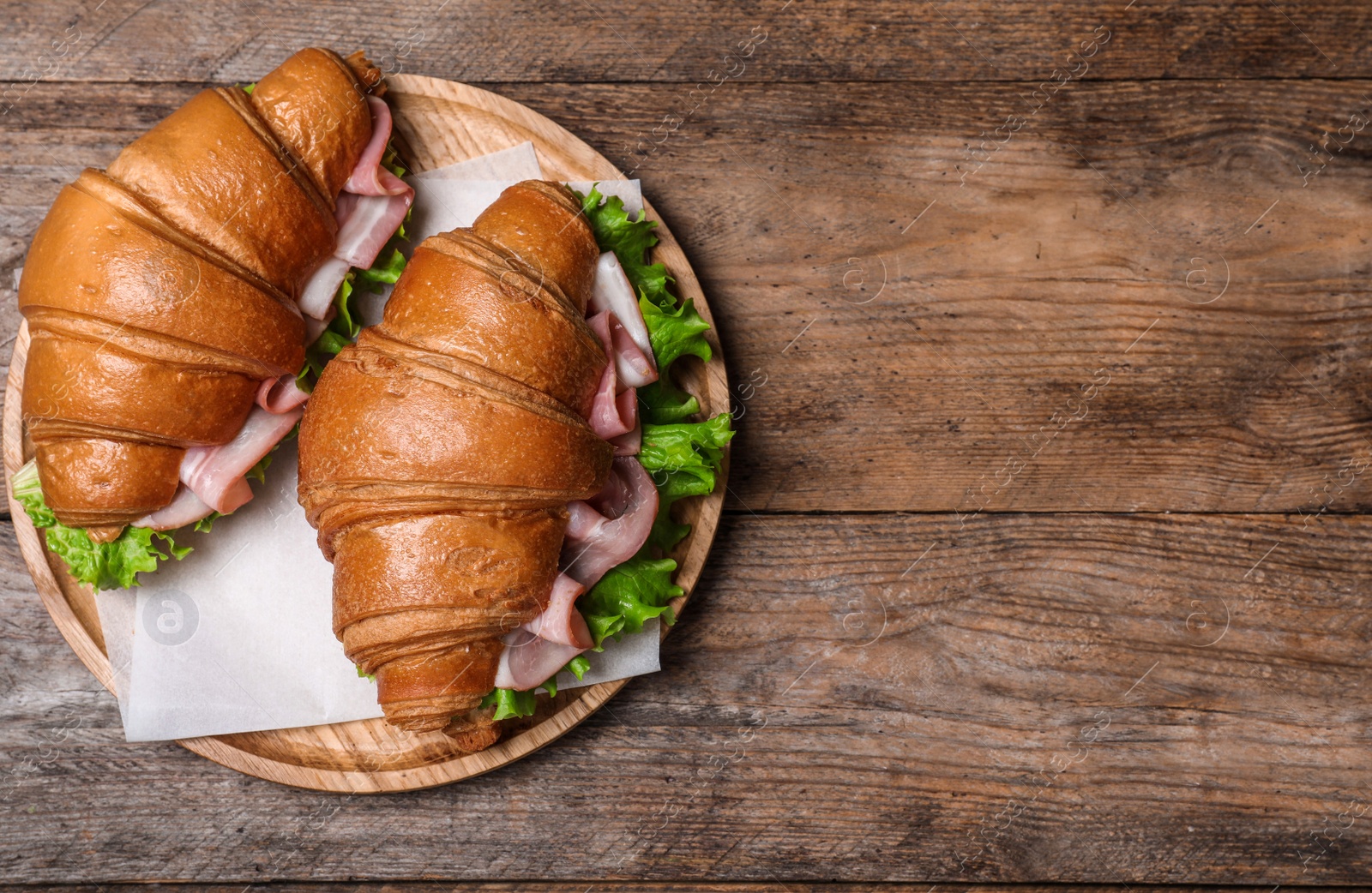 Photo of Tasty croissant sandwiches with ham on wooden table, top view. Space for text