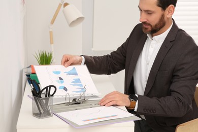 Businessman putting document into file folder at white table in office
