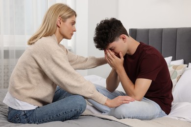 Photo of Mother consoling her upset son in bedroom. Teenager problems