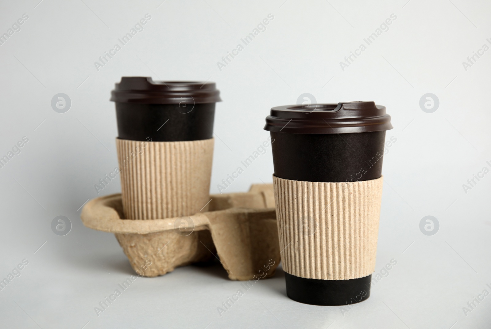 Photo of Takeaway paper coffee cups with sleeves, plastic lids and cardboard holder on grey background