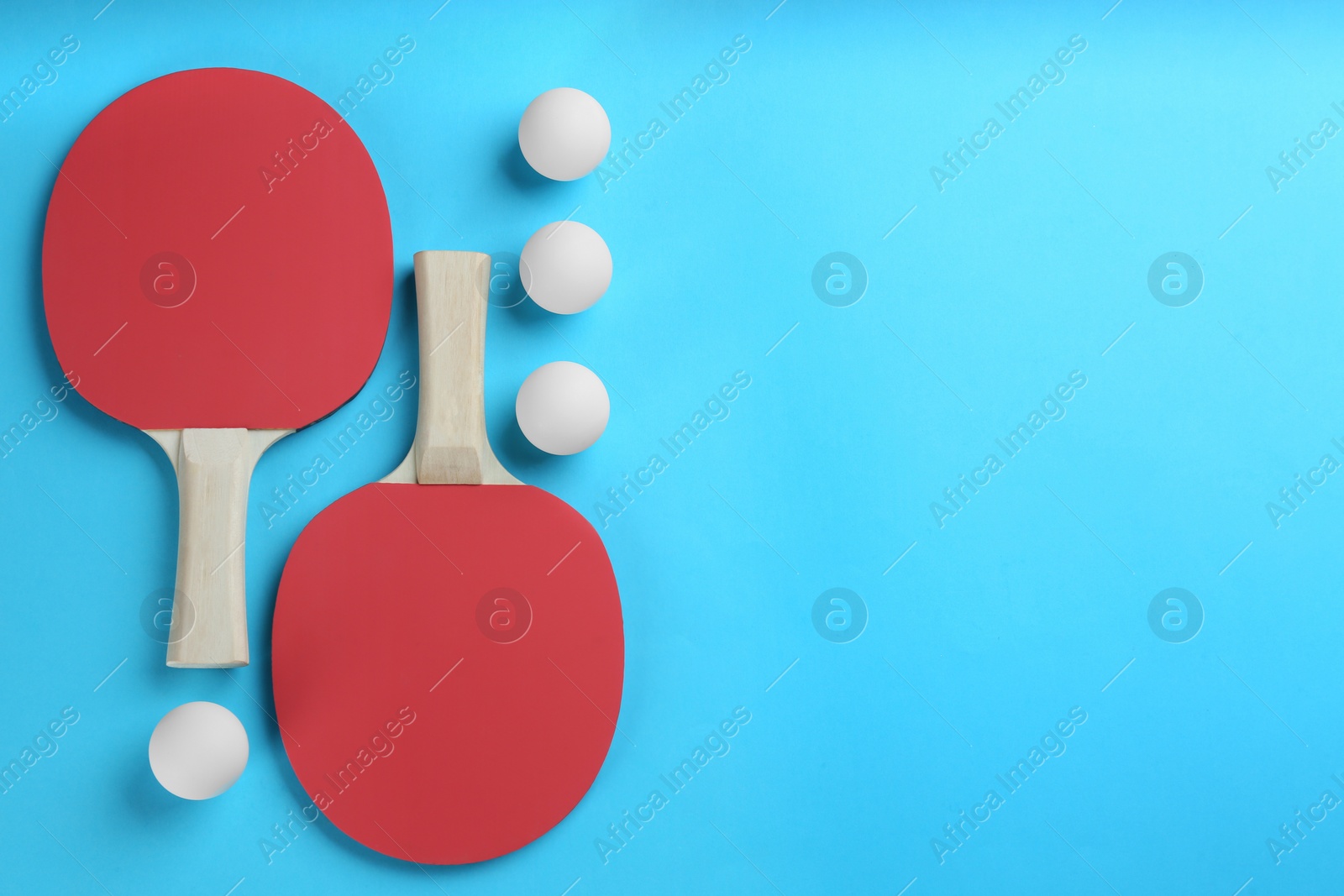 Photo of Ping pong rackets and balls on light blue background, flat lay. Space for text
