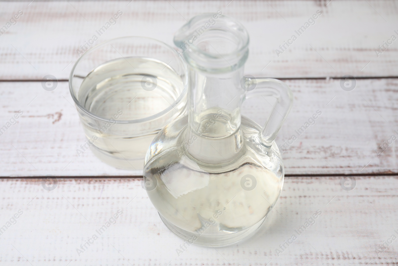 Photo of Vinegar in glass jug and bowl on white wooden table