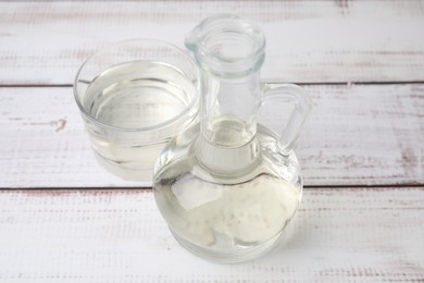 Photo of Vinegar in glass jug and bowl on white wooden table