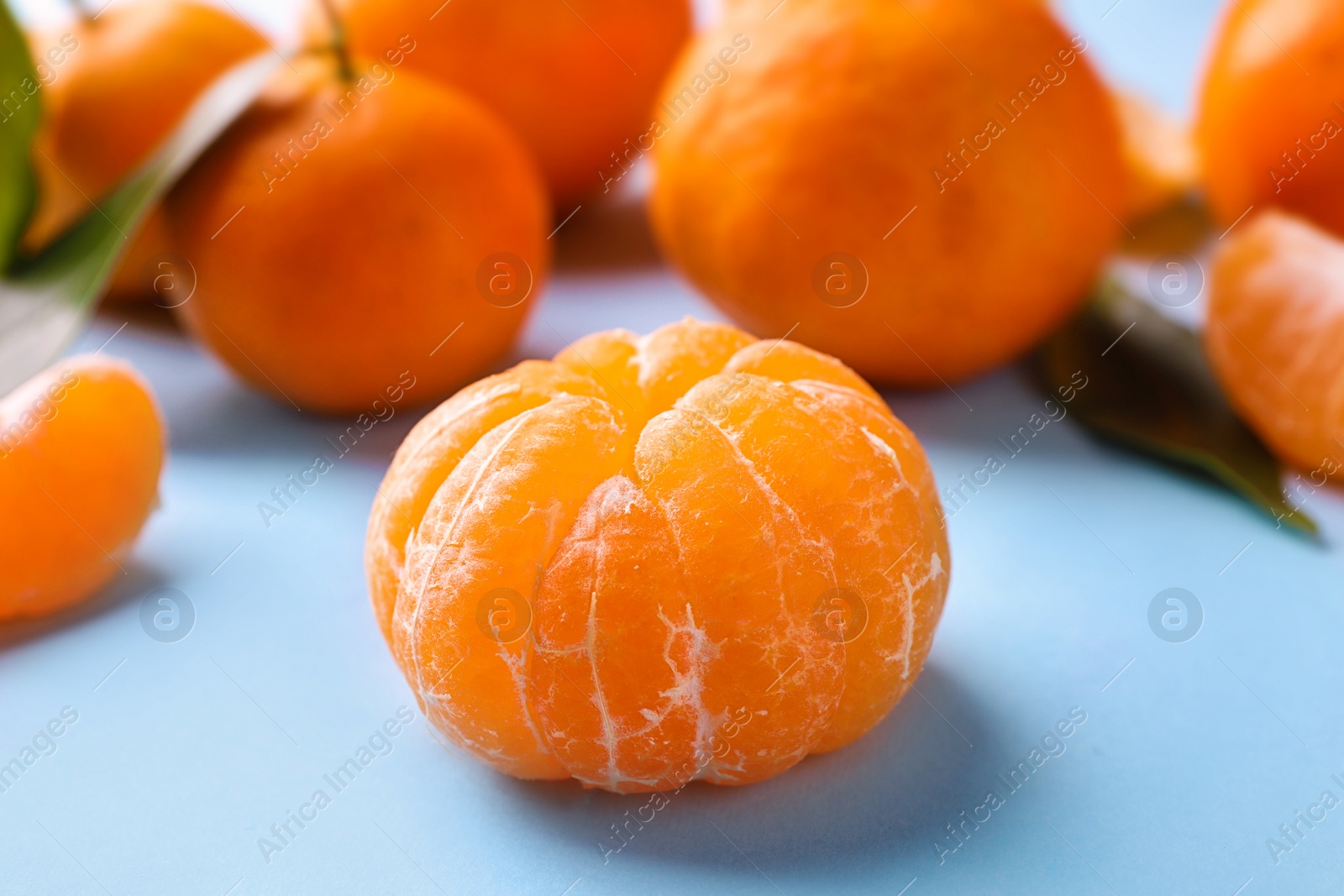 Photo of Peeled fresh ripe tangerine on light blue background, closeup