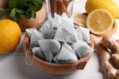 Photo of Tea bags, mint, lemons and ginger on white wooden table, closeup