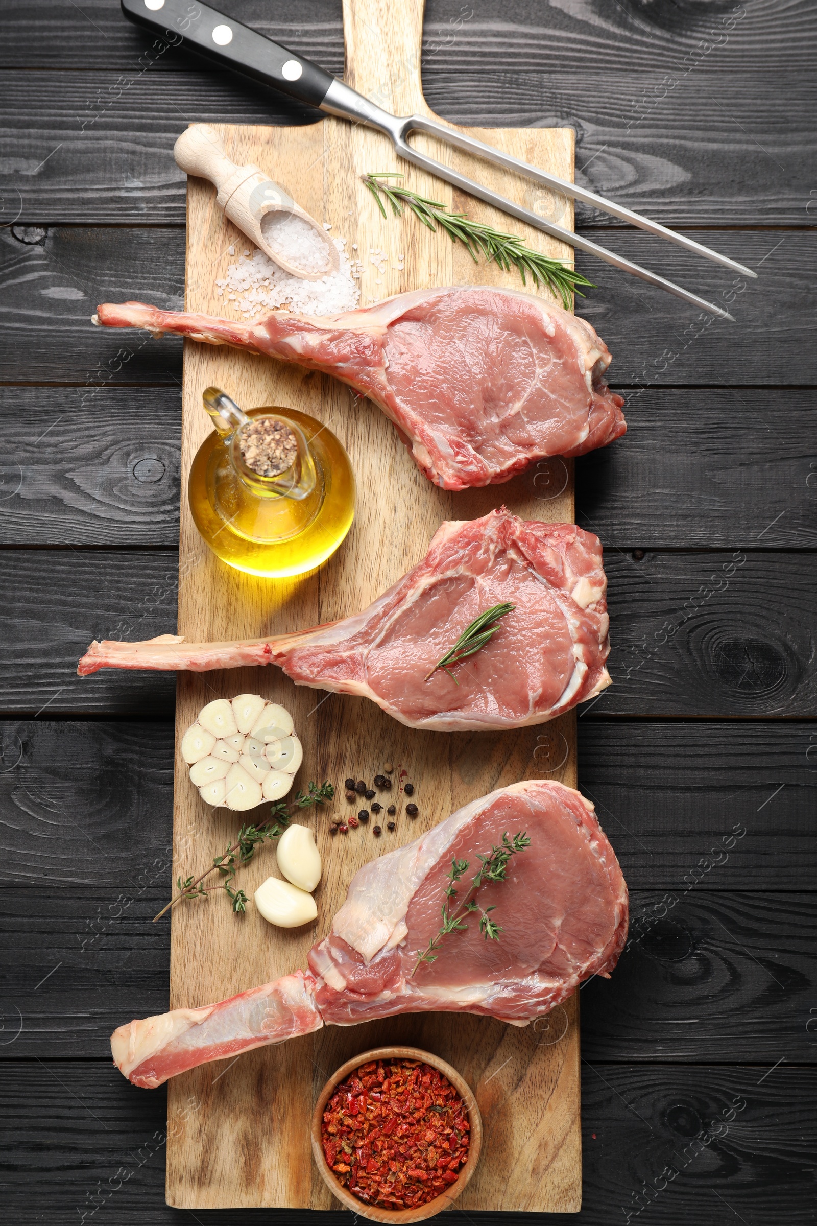 Photo of Fresh tomahawk beef cuts, spices and butcher fork on black wooden table, top view