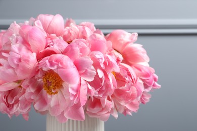 Beautiful bouquet of pink peonies in vase near grey wall, closeup