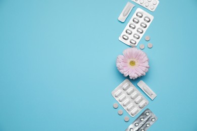 Many gynecological pills and gerbera flower on light blue background, flat lay. Space for text