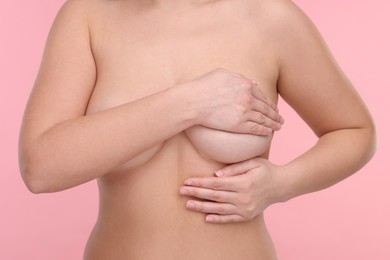 Photo of Mammology. Naked woman doing breast self-examination on pink background, closeup