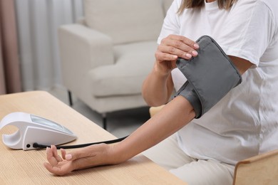 Woman measuring blood pressure at wooden table in room, closeup