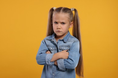 Photo of Resentful girl with crossed arms on orange background