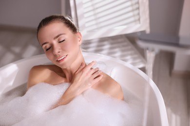 Photo of Beautiful woman taking bath in tub with foam indoors. Space for text