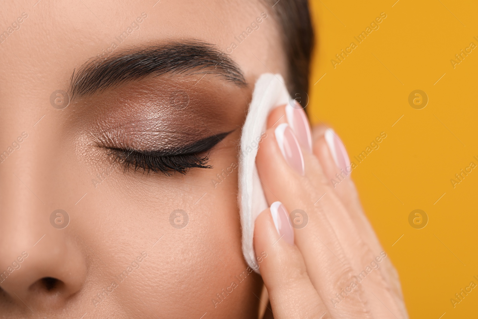 Photo of Beautiful woman removing makeup with cotton pad on orange background, closeup. Space for text