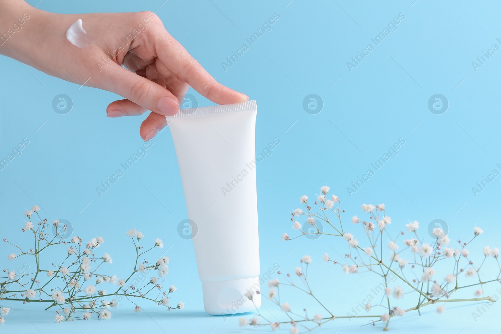 Photo of Woman with tube of cream and flowers on light blue background, closeup