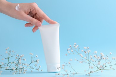 Woman with tube of cream and flowers on light blue background, closeup