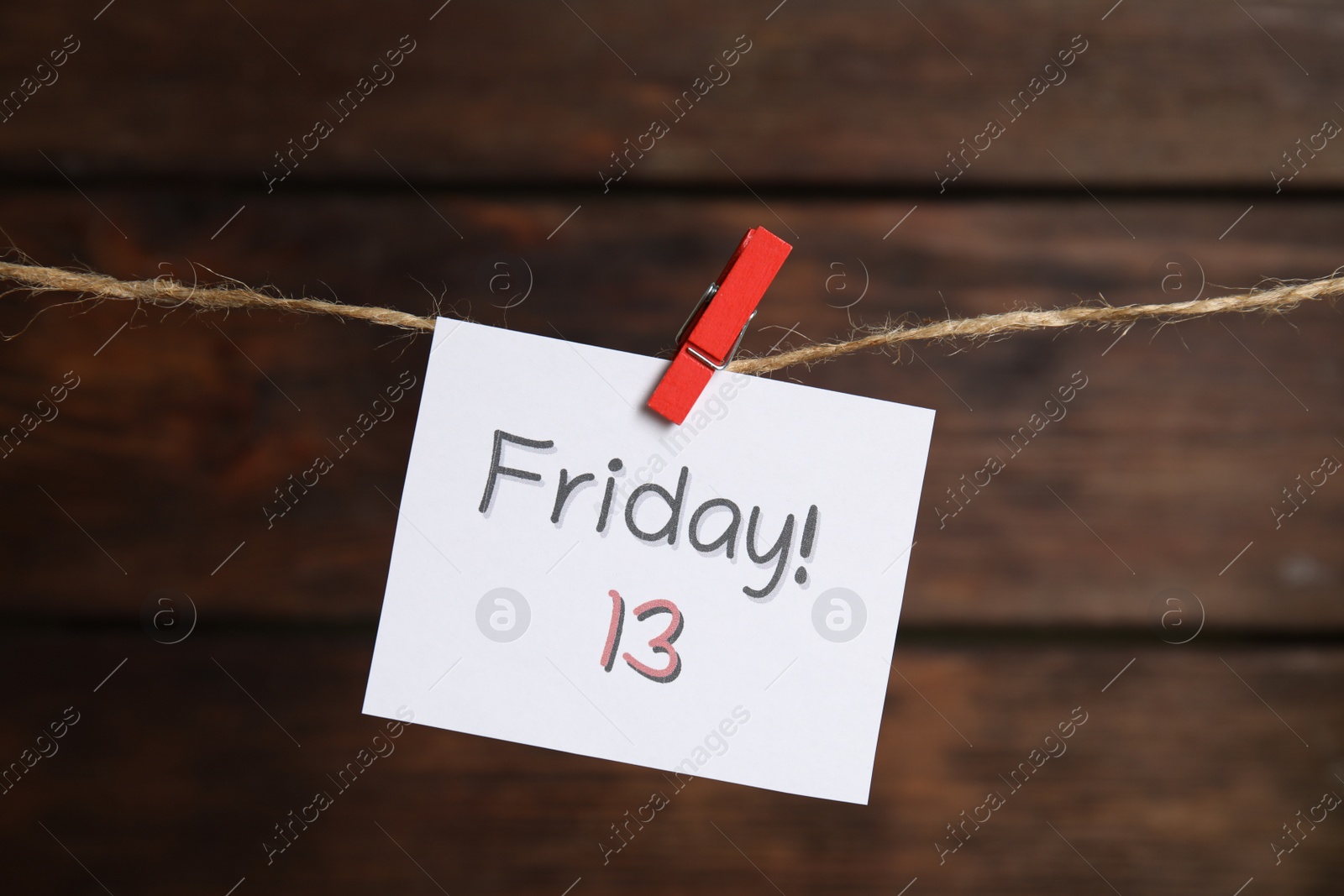 Photo of Paper note with phrase Friday! 13 hanging on twine against wooden background. Bad luck superstition