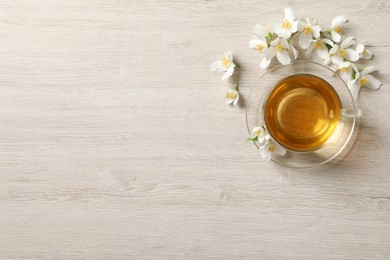Photo of Glass cup of aromatic jasmine tea and fresh flowers on light wooden table, flat lay. Space for text