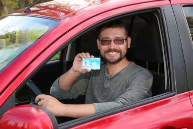 Photo of Happy man showing driving license from car