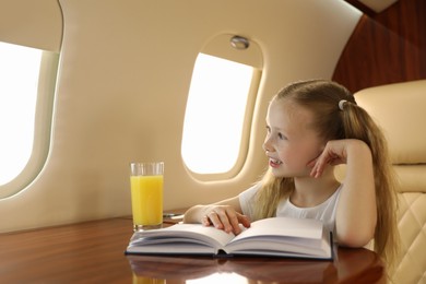 Photo of Cute little girl reading book at table in airplane during flight
