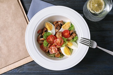 Photo of Plate with delicious fresh salad and menu on table, top view