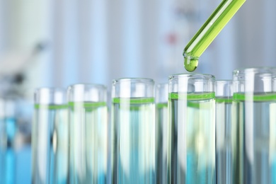 Photo of Dripping liquid into test tube on blurred background, closeup. Laboratory analysis