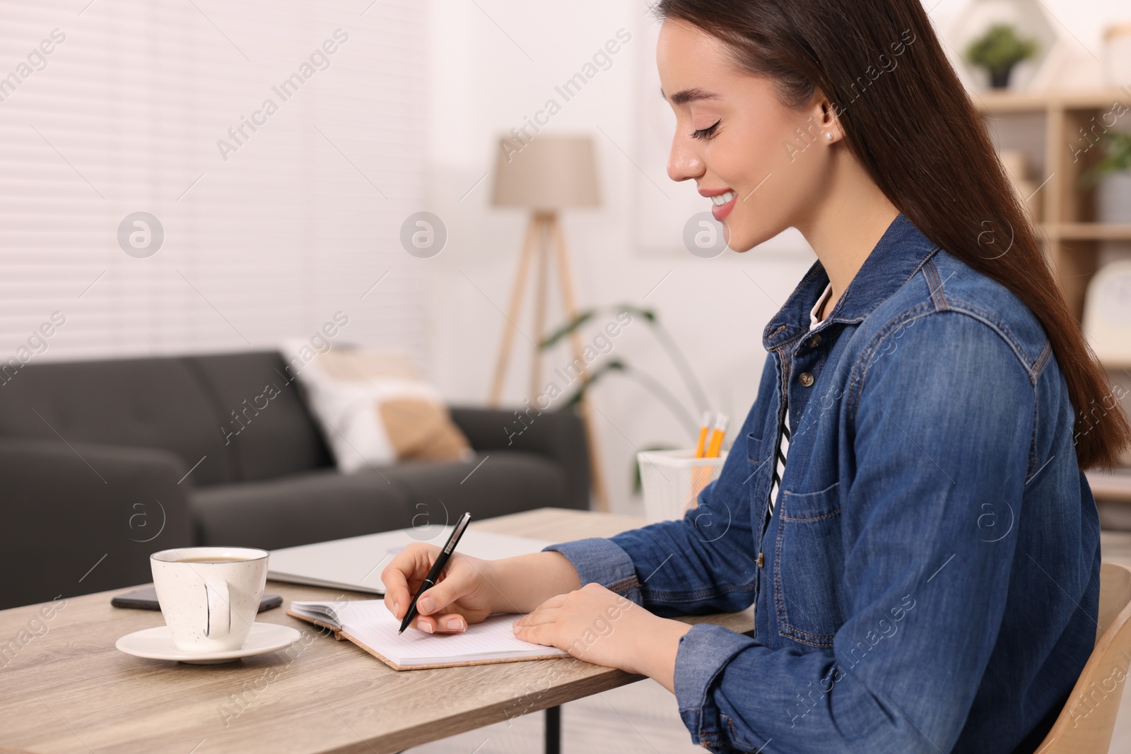 Photo of Young woman writing in notebook at wooden table indoors