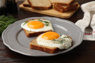 Plate with tasty fried eggs, slices of bread and dill on dark wooden table, closeup