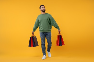 Smiling man with many paper shopping bags on orange background