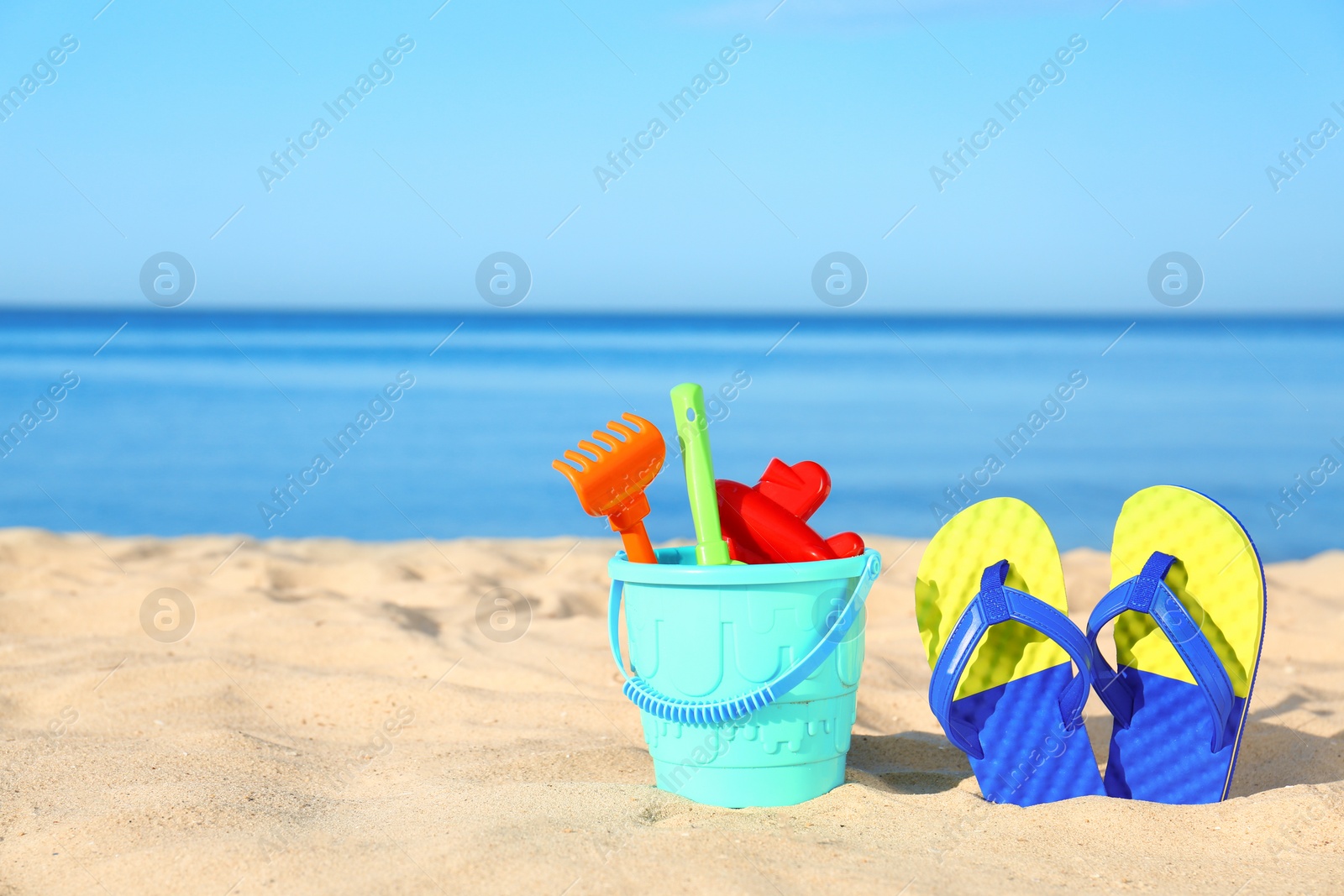 Photo of Beautiful view of sand with plastic beach toys and flip flops near sea on sunny day. Space for text