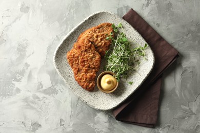 Photo of Tasty schnitzels served with sauce and microgreens on grey textured table, top view
