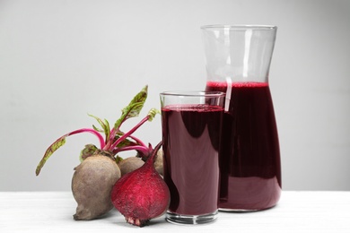 Photo of Fresh beet juice and raw vegetable on white wooden table