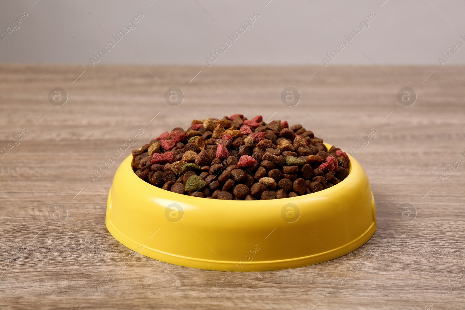 Photo of Dry food in yellow pet bowl on wooden surface