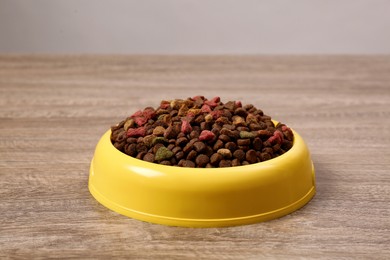 Dry food in yellow pet bowl on wooden surface