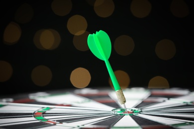 Green arrow hitting target on dart board against blurred lights