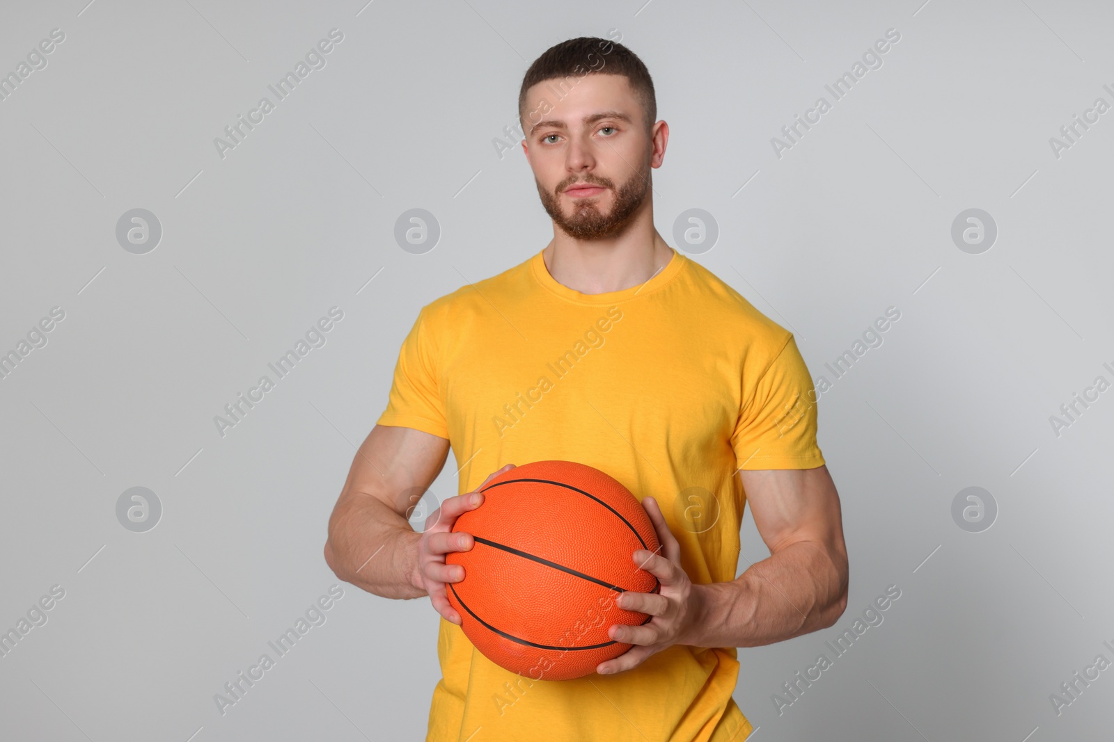 Photo of Athletic young man with basketball ball on light grey background