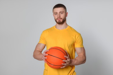 Athletic young man with basketball ball on light grey background