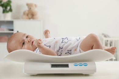 Photo of Cute little baby lying on scales in light room