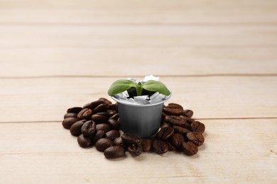 Photo of Green seedling growing in coffee capsule and beans on wooden table, space for text