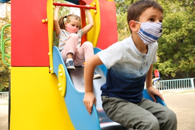 Little children with medical face masks on playground during covid-19 quarantine