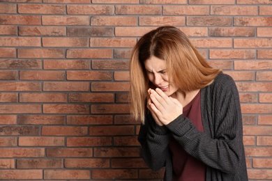 Photo of Woman suffering from cold near brick wall. Space for text