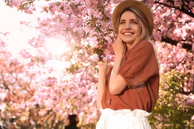 Photo of Young woman wearing stylish outfit near blossoming sakura in park. Fashionable spring look
